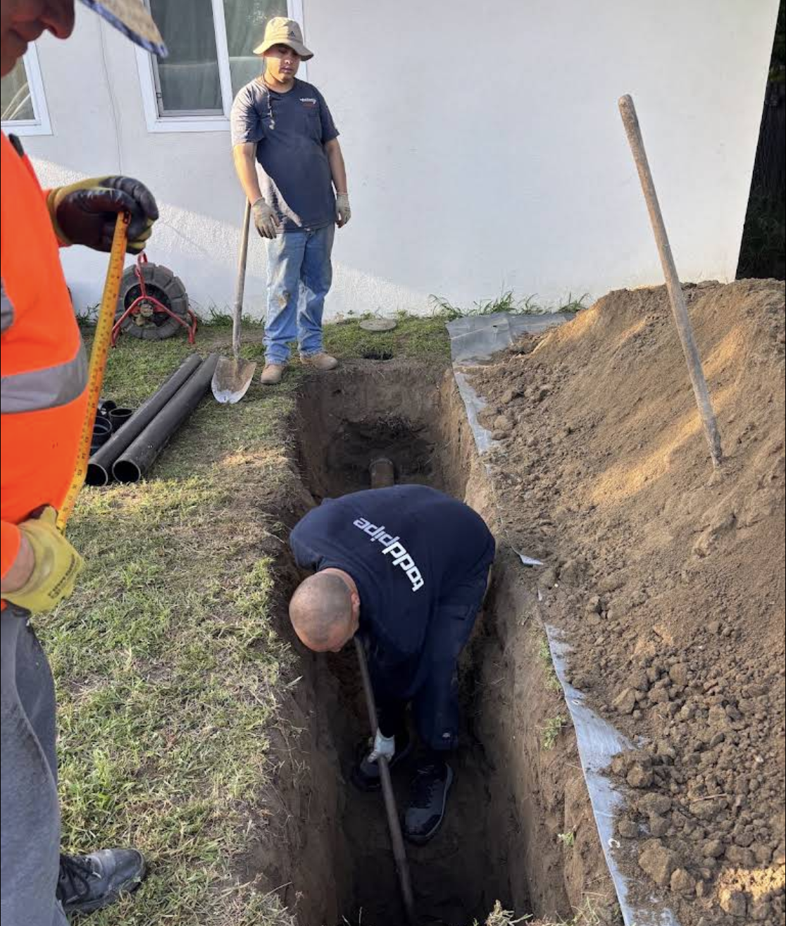 Construction worker digging trench with shovel while supervisor watches on job site