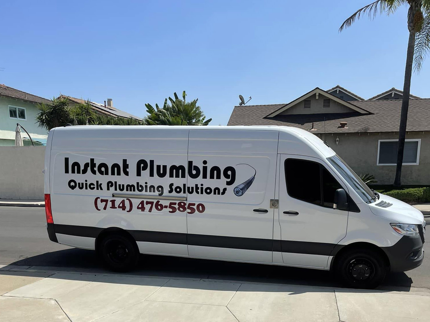 White plumbing service van with "Instant Plumbing" branding and phone number parked on residential street