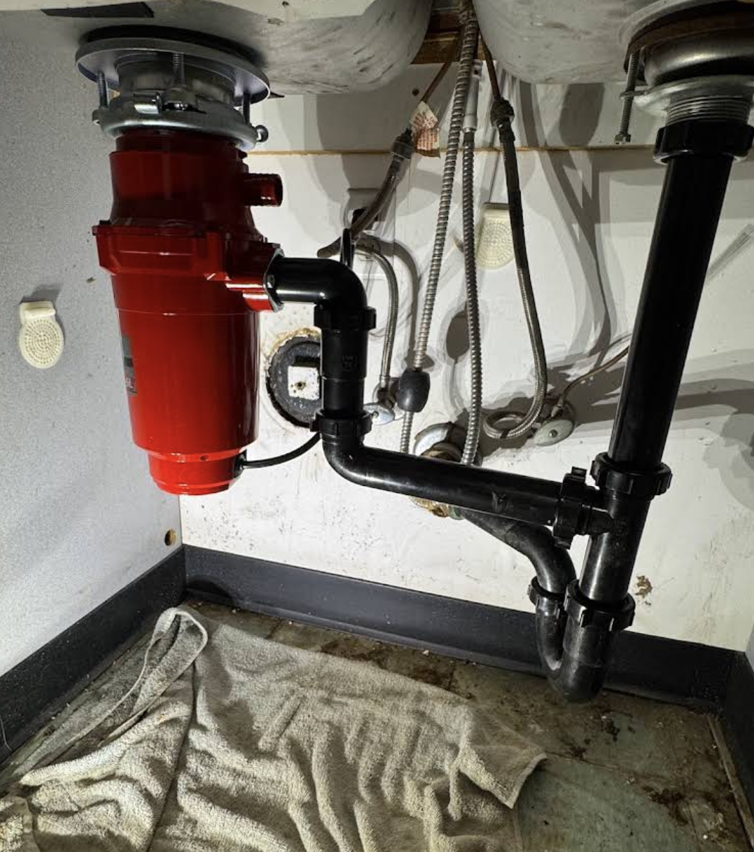Under-sink plumbing with red garbage disposal unit and black drain pipes