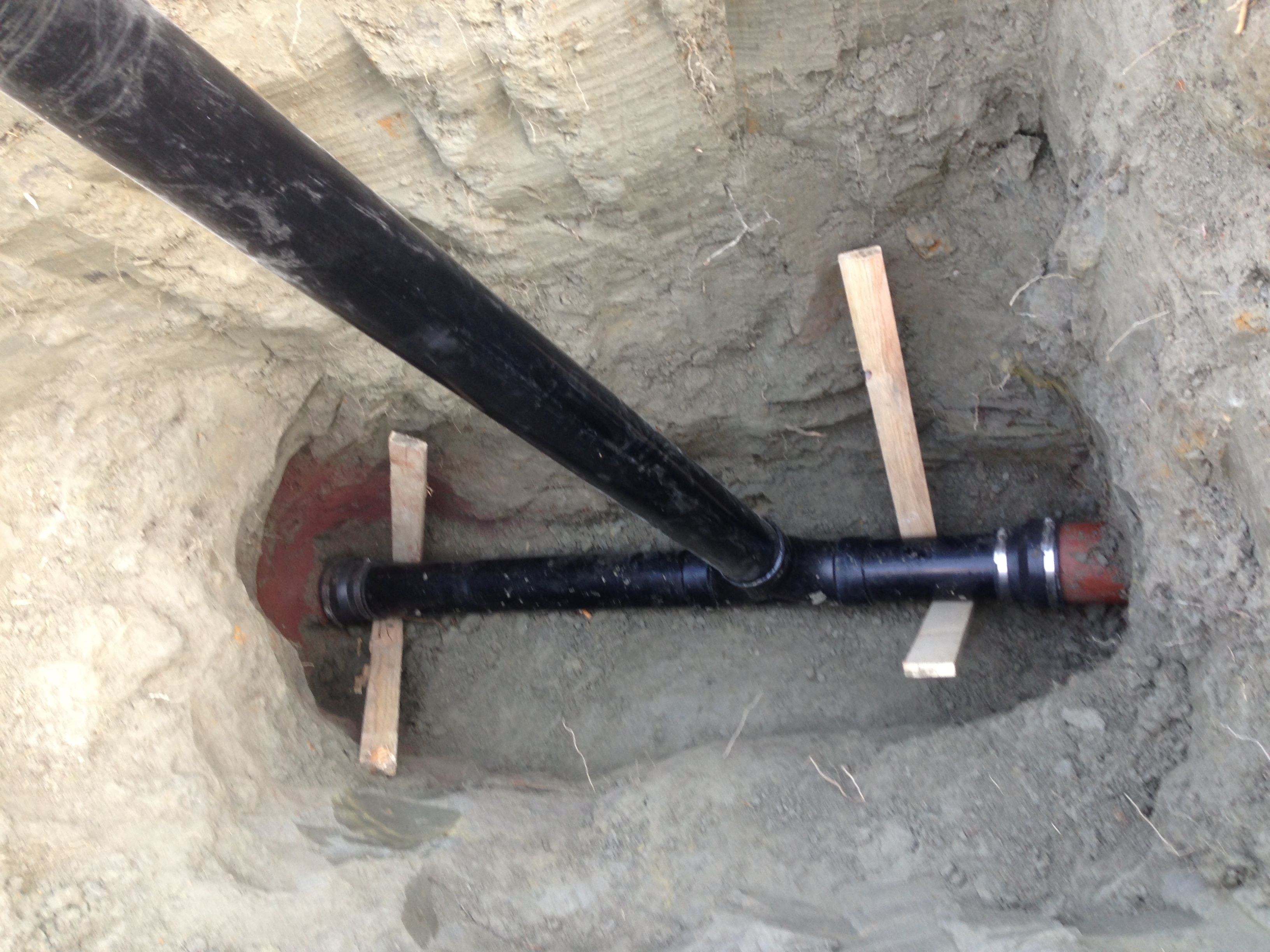 Buried black pipe with red valve fitting and wooden bracing in concrete ground