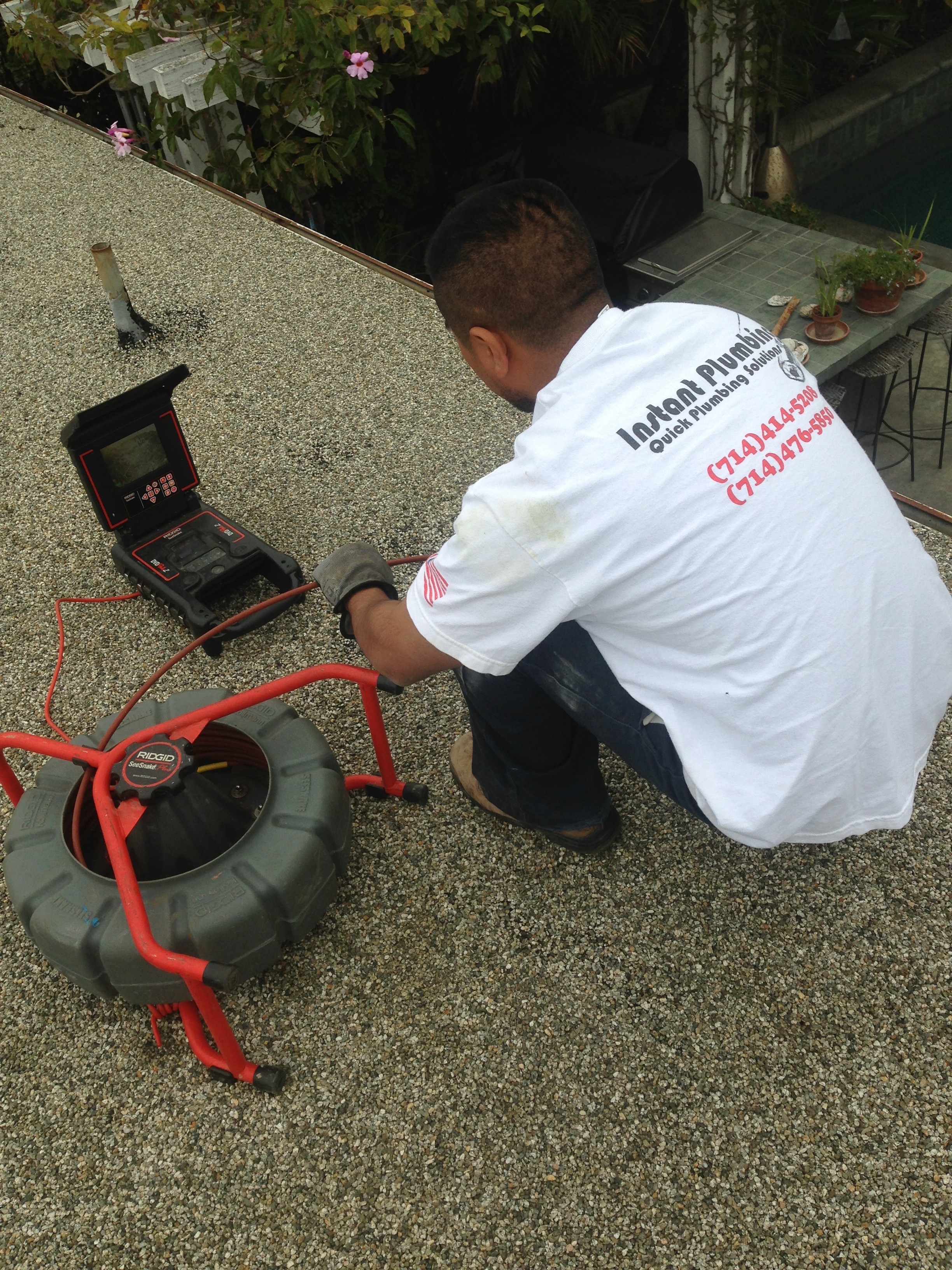 Technician in white shirt using digital multimeter to test red electrical equipment on concrete surface