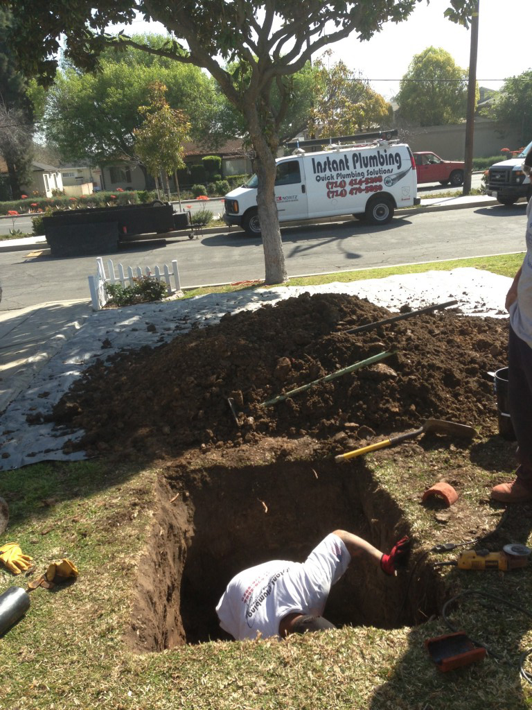 Plumber working in excavated trench on residential street with service van parked nearby