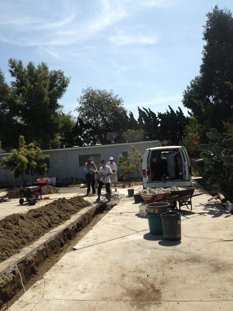 Construction workers and white van at residential job site with excavated trench