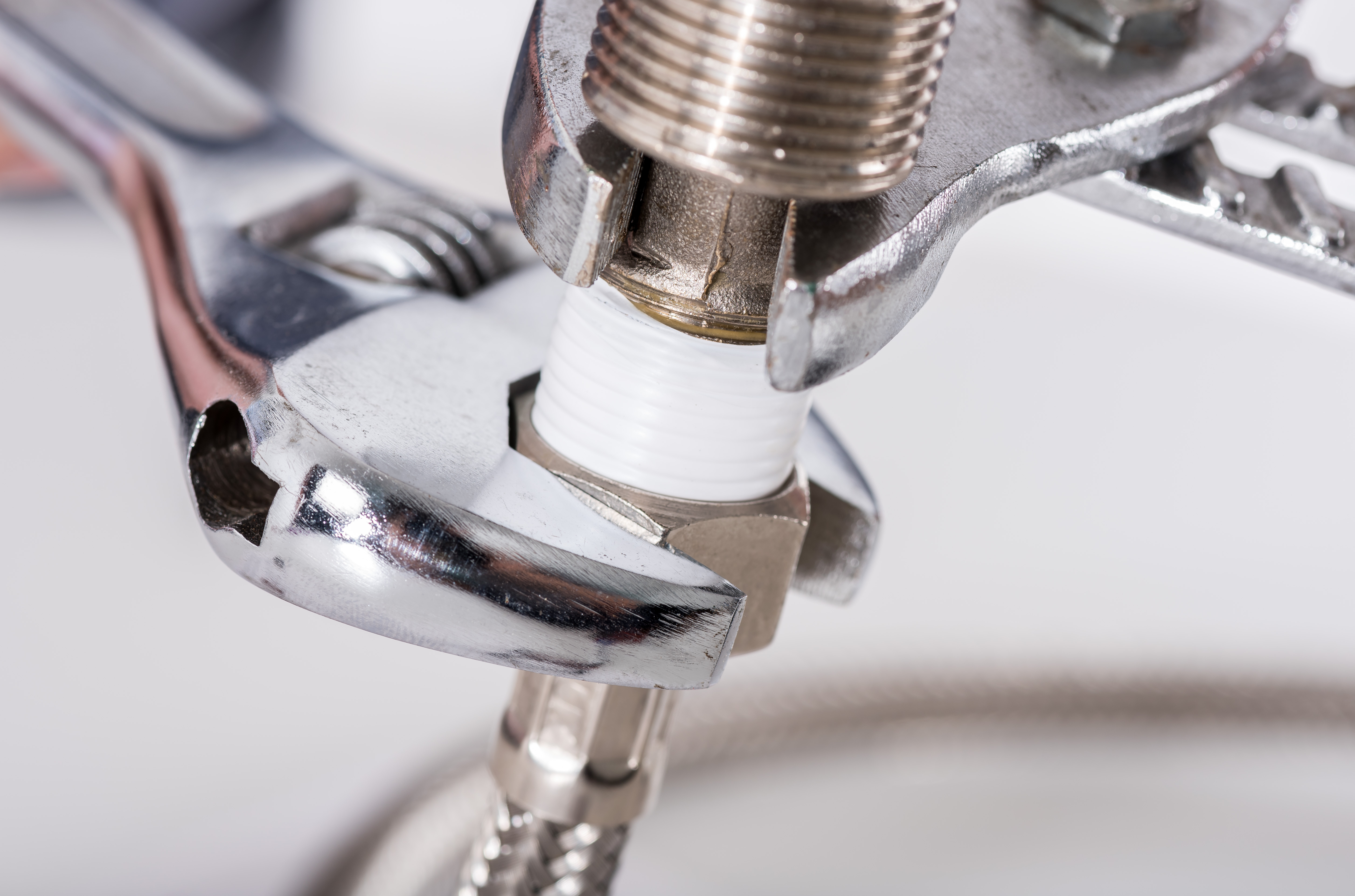 Wrench tightening a chrome pipe fitting with white threaded connector