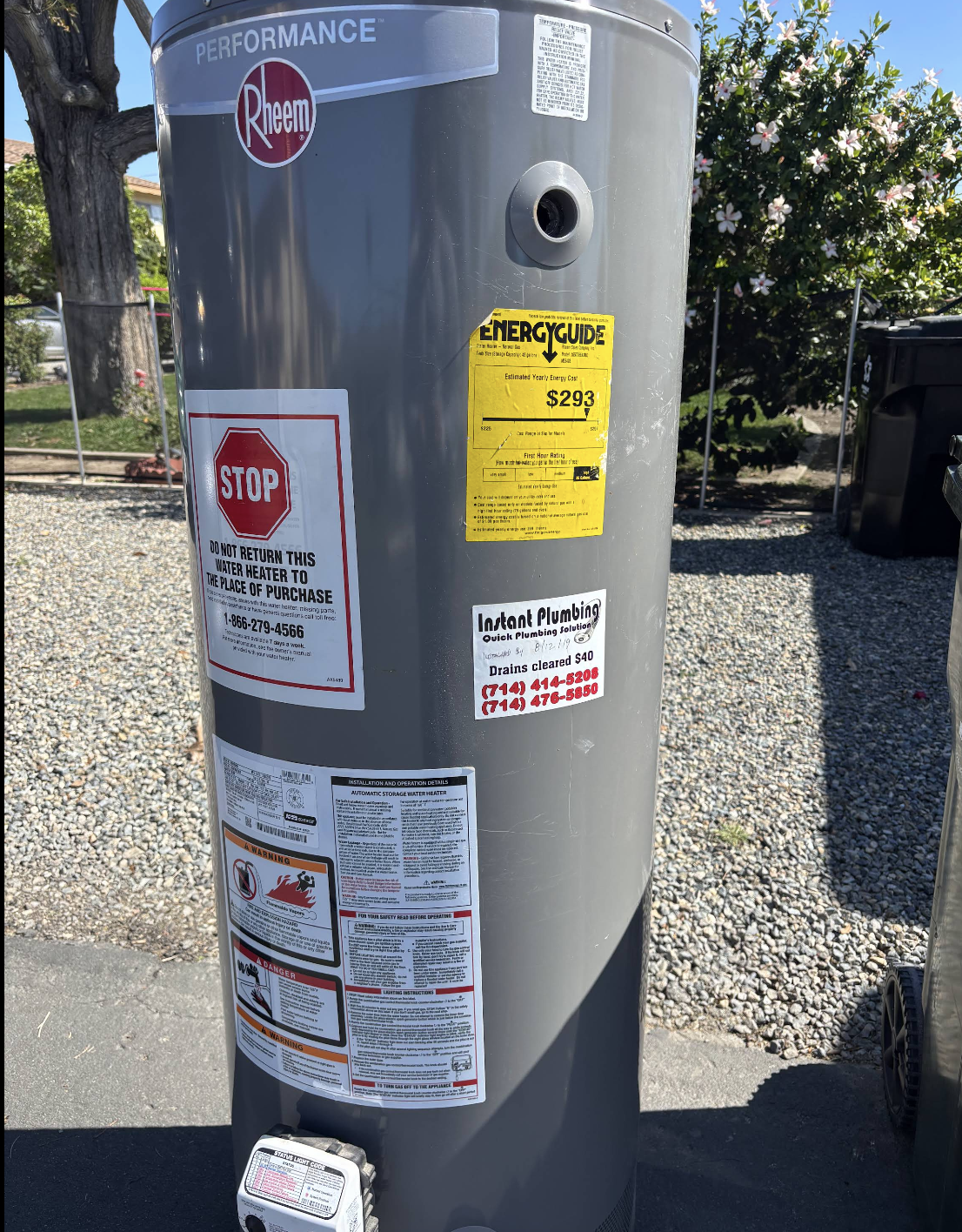 Rheem Performance water heater with Energy Guide label and Instant Plumbing service stickers in outdoor setting