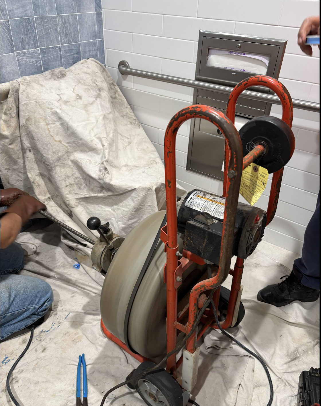 Red motorized pipe stripping machine in bathroom with white subway tiles and towel rack
