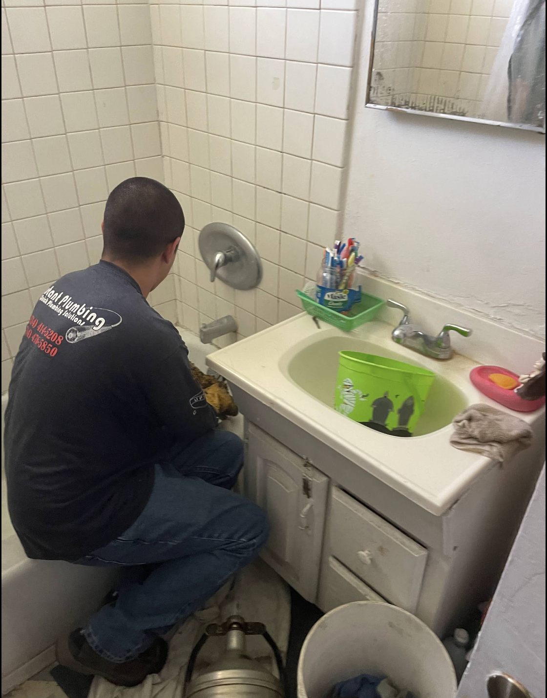 Plumber crouched at bathroom sink inspecting plumbing fixtures and drain