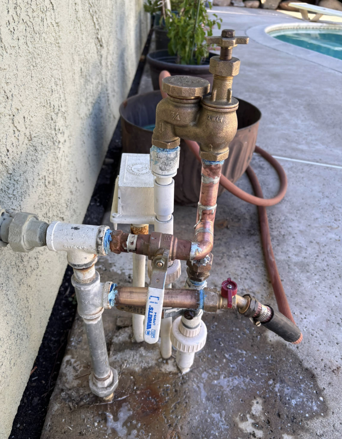Pool equipment manifold with brass valves, gauges, and white PVC fittings installed against concrete wall